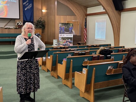 Kathy Marson stands in a church with pews behind her, speaking into a microphone.